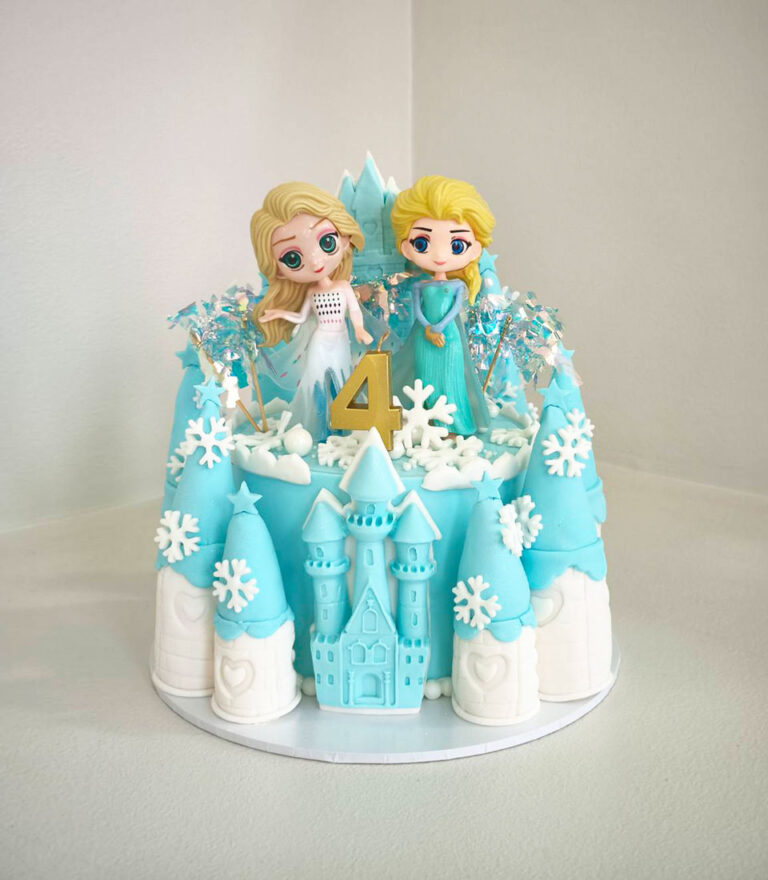 Frozen-themed fondant birthday cake with handcrafted Elsa and Anna figures on a blue castle design by Charlotte Bakery in Bangkok.