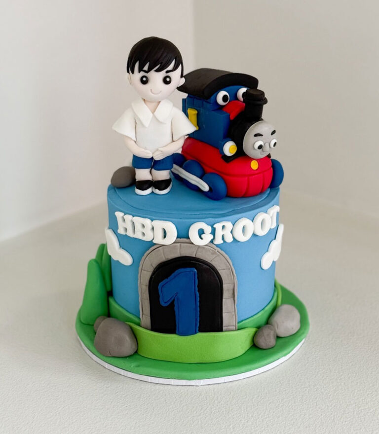 Train-themed fondant birthday cake with Thomas-style train and child figure by Charlotte Bakery in Bangkok.