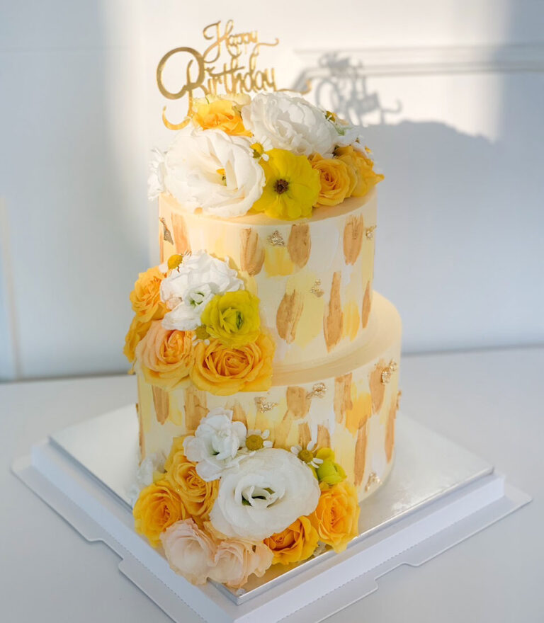 Two-tier birthday cake with yellow floral decorations by Charlotte Bakery in Bangkok