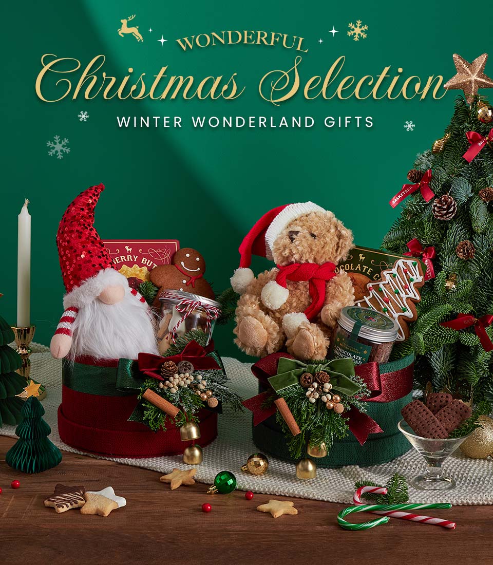 Festive display featuring two hampers with a gnome and a teddy bear, surrounded by Christmas decorations, biscuits, a candle, and a small decorated Christmas tree. Text reads: “Wonderful Christmas Selection.”.