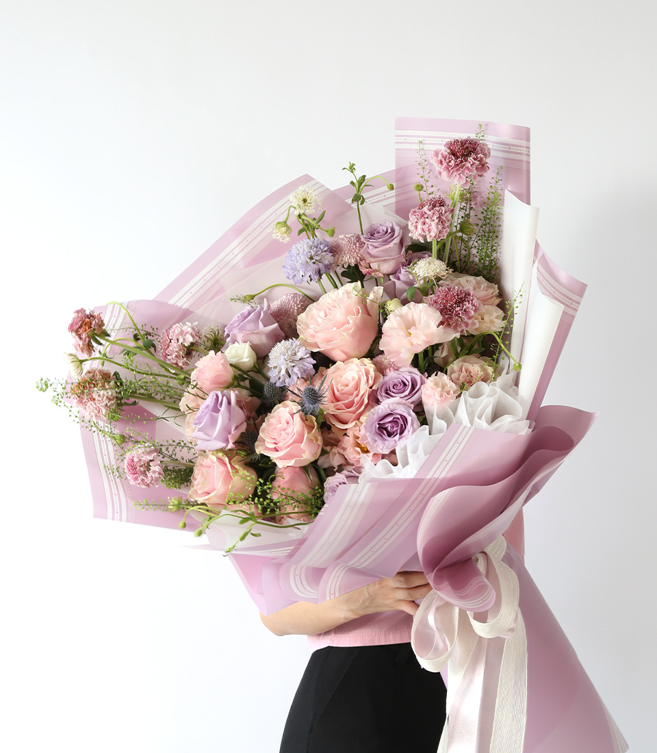 Pastel pink and lavender garden-style bouquet with roses and seasonal blooms, wrapped in soft pink paper in Bangkok.