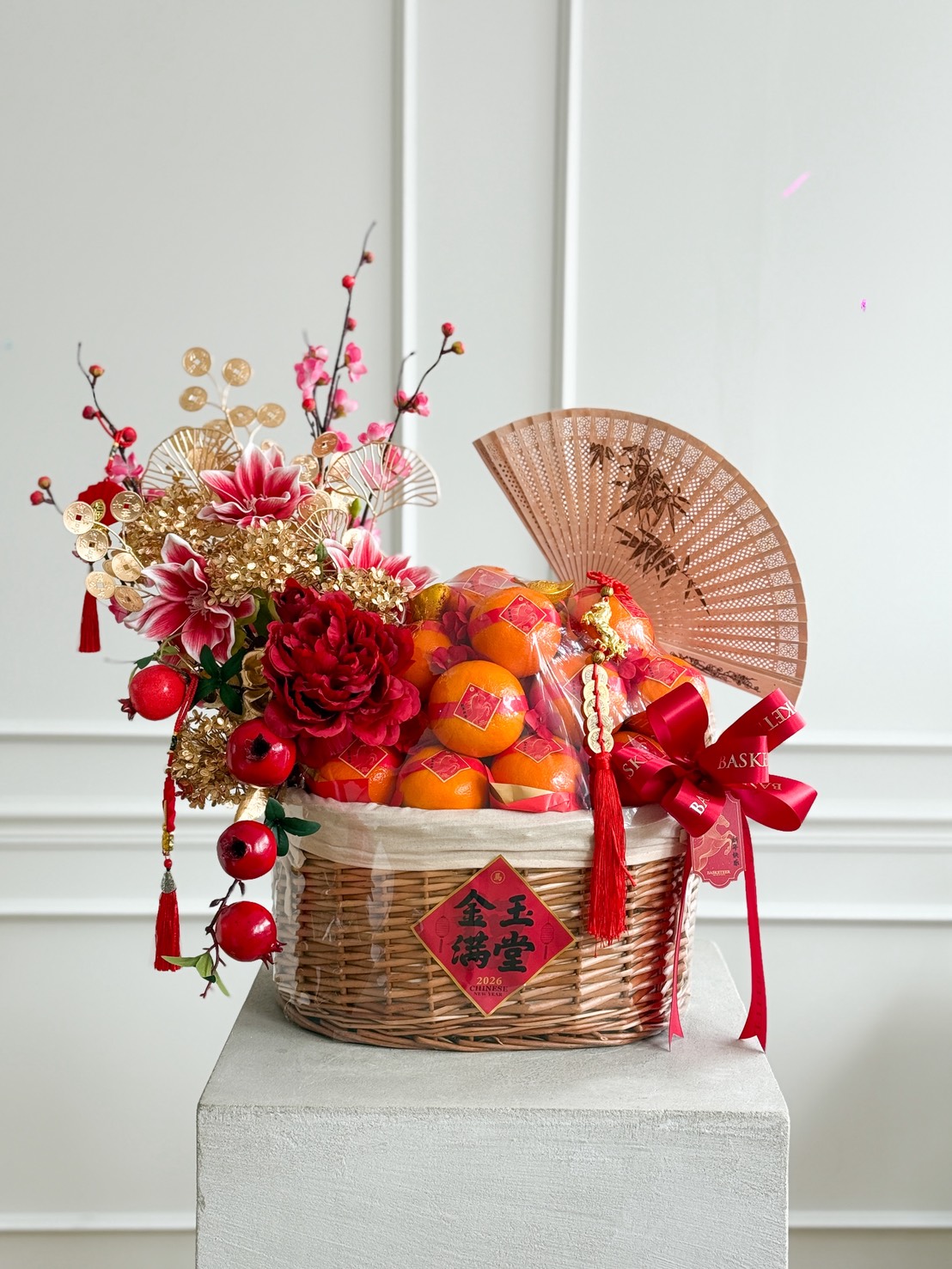 A festive Chinese New Year Mandarin Orange Hamper with Bamboo Fan, decorated with red and gold flowers, artificial cherry blossoms, red ribbons, and a diamond-shaped label with Chinese characters for good fortune.