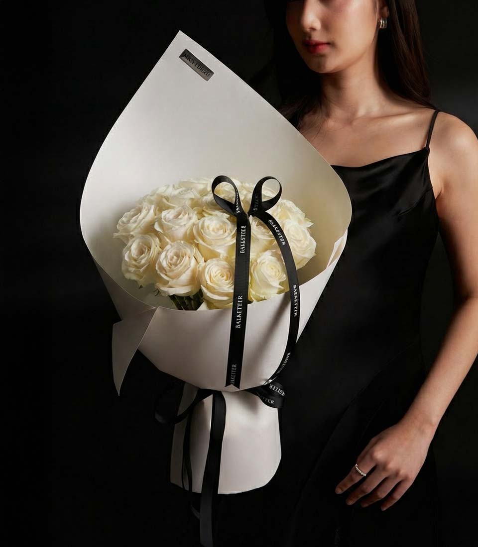 A beautiful white rose bouquet for Valentine gift delivery in Bangkok SKU VLT26-2023lFront view of a model holding a luxury white rose bouquet in modern sculptural wrappinglClose-up of fresh white roses in a premium Valentine arrangement with a black ribbonlSophisticated white rose bouquet with architectural paper styling