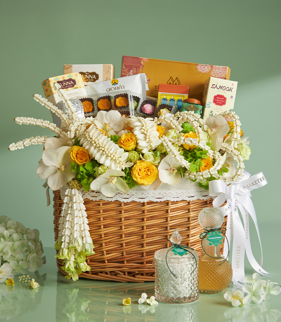 A Homepage Select wicker hamper, decorated with white and yellow flowers, contains assorted snacks, chocolates, and packaged treats—ideal for Popular Occasions. Beside it are two glass jars: one with honey and one with a clear liquid.